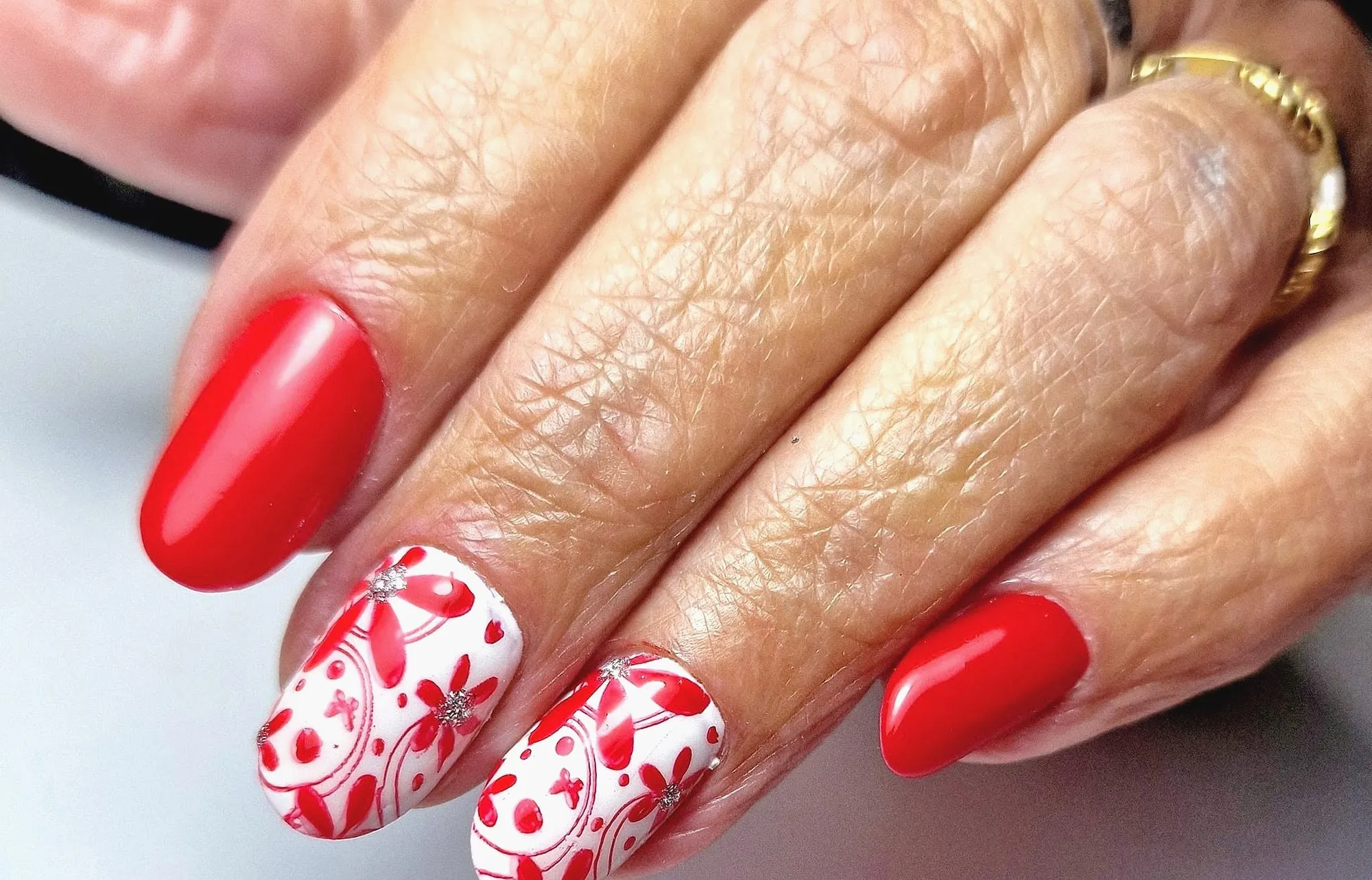 Rode ovale nagels en twee witte nagels met rode getekende bloemen